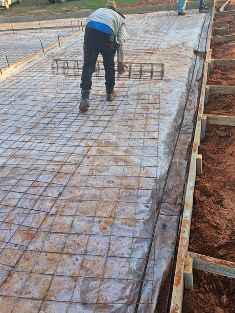 Construction worker in blue shirt laying steel reinforcement mesh on concrete foundation at construction site