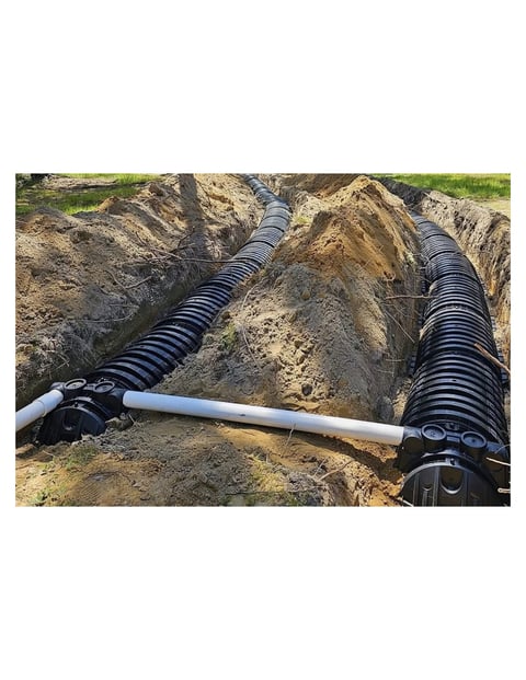 Drainage pipes being installed in an excavated trench with white connector joint and black corrugated tubing visible