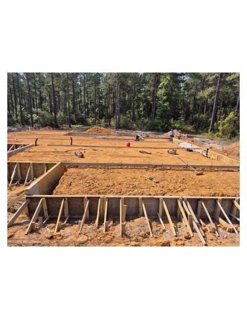 Construction site with wooden foundation framing and workers preparing building foundation in cleared forest area