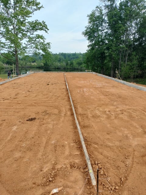 Newly cleared dirt lot with center line marking, bordered by trees and water in background